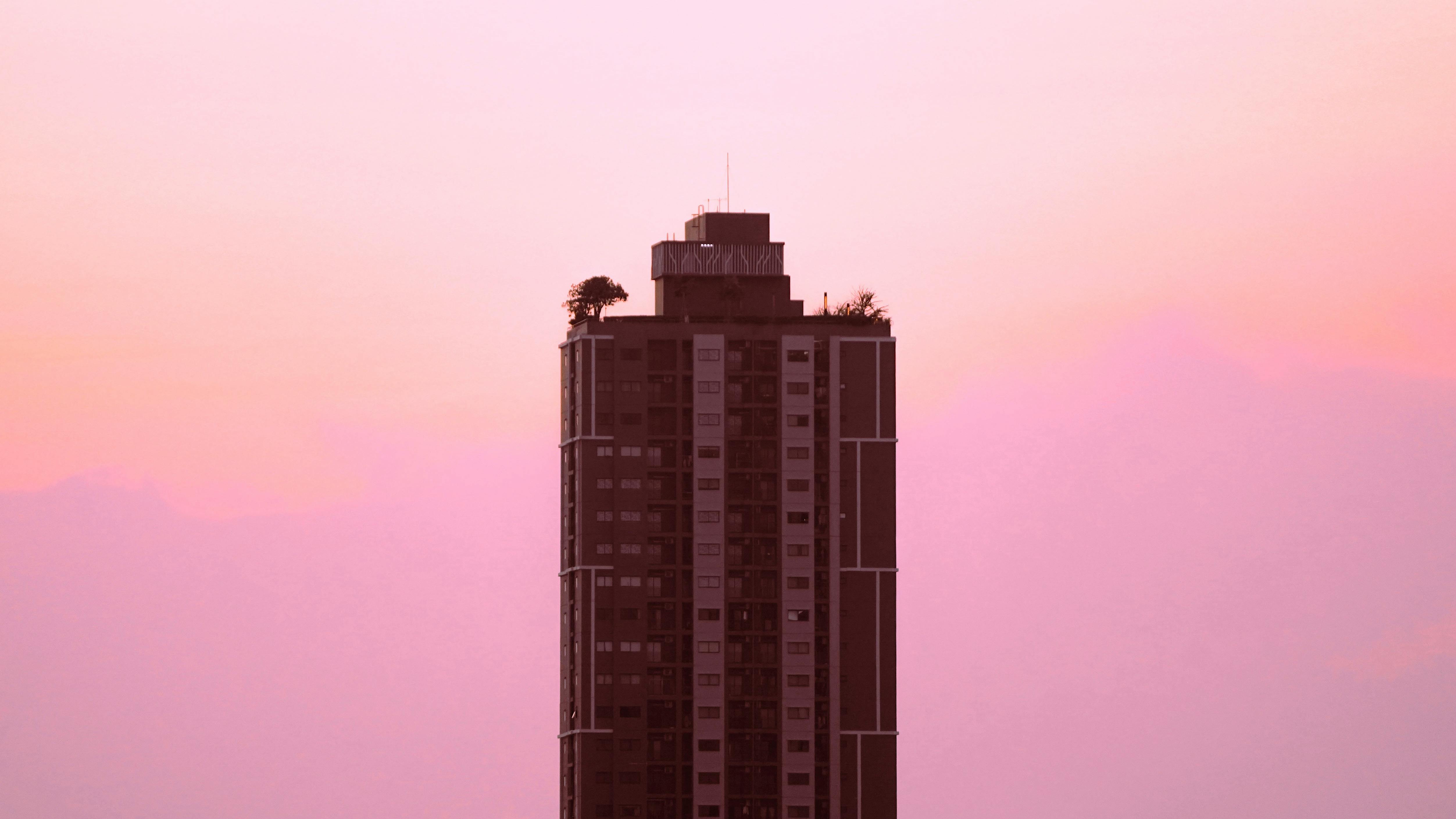 A striking view of a modern skyscraper against a vibrant pink sky during sunset in Nonthaburi, Thailand.