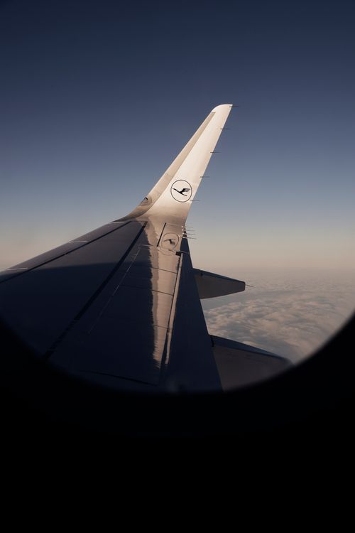 Free View from airplane window showing the aircraft wing and clouds below during flight at higher altitude. Stock Photo