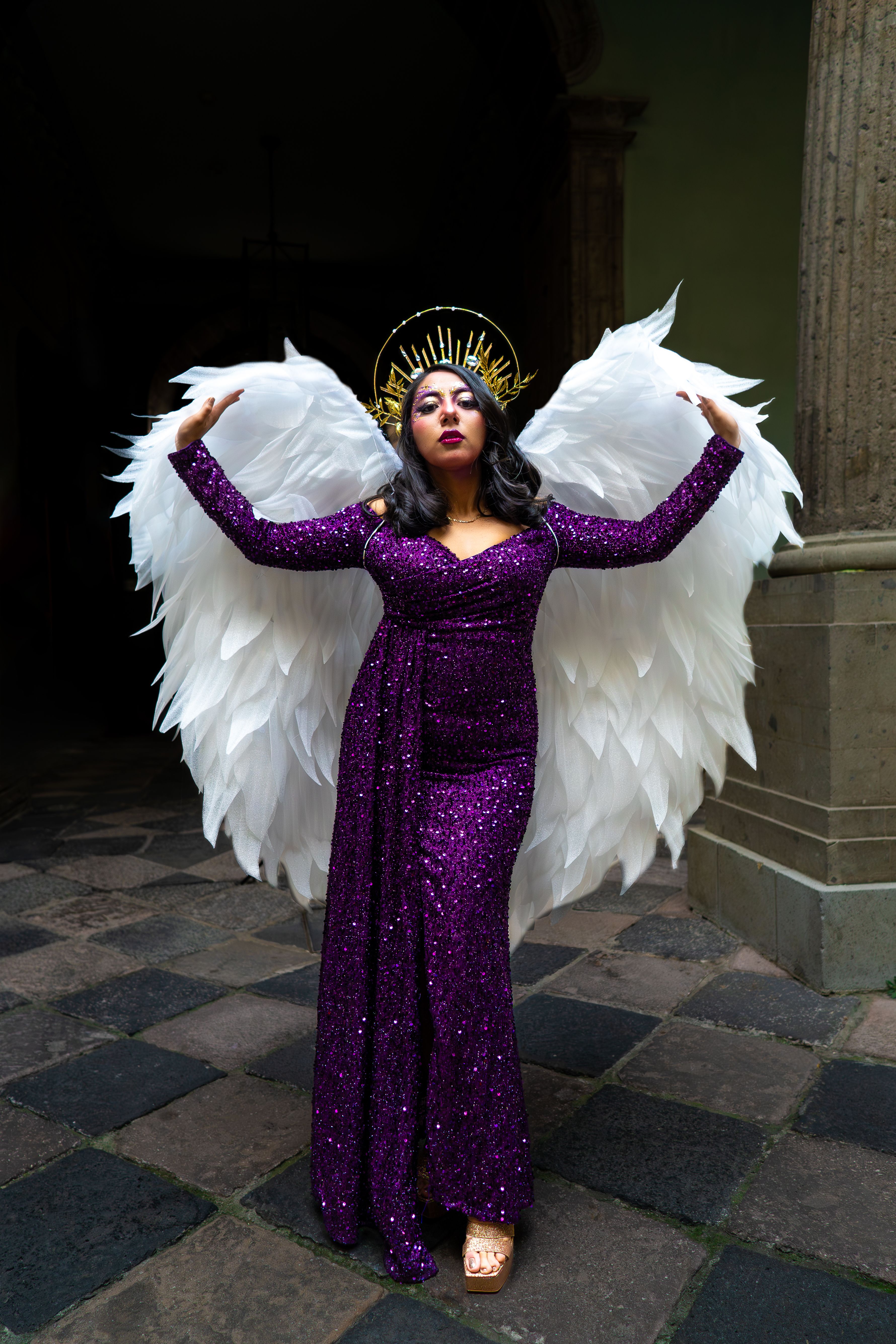 A woman in a purple dress and angel wings poses confidently indoors.