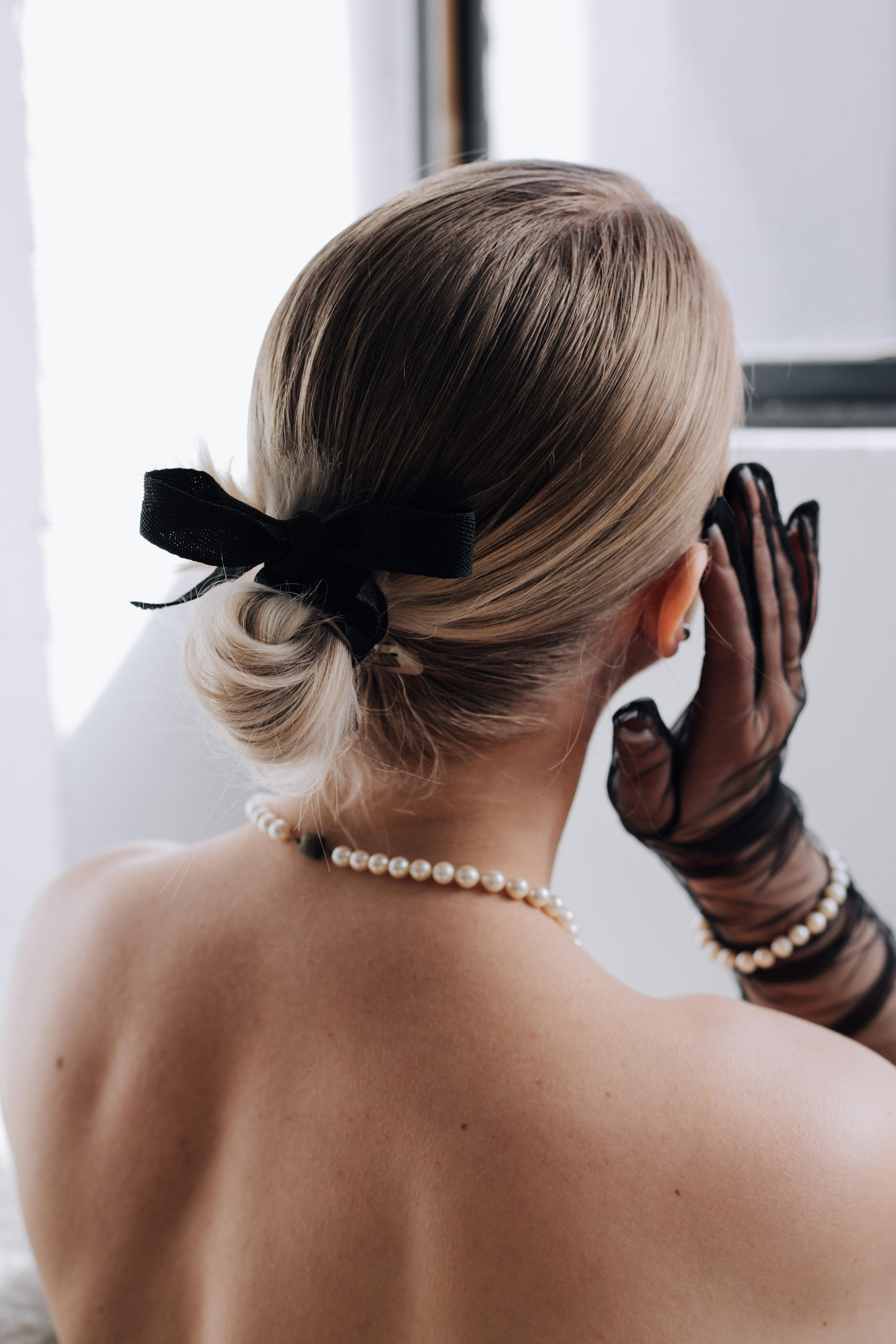 Back view of an elegant woman wearing a pearl necklace and black mesh gloves, showcasing grace.