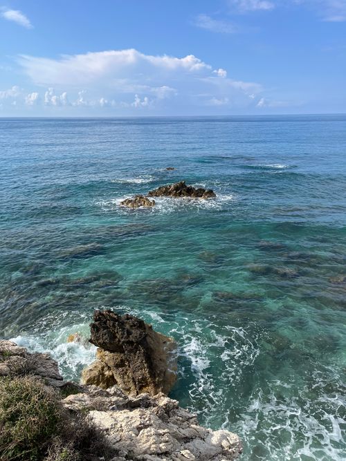 Free Captivating view of rocky coast with turquoise ocean and waves under a blue sky. Stock Photo