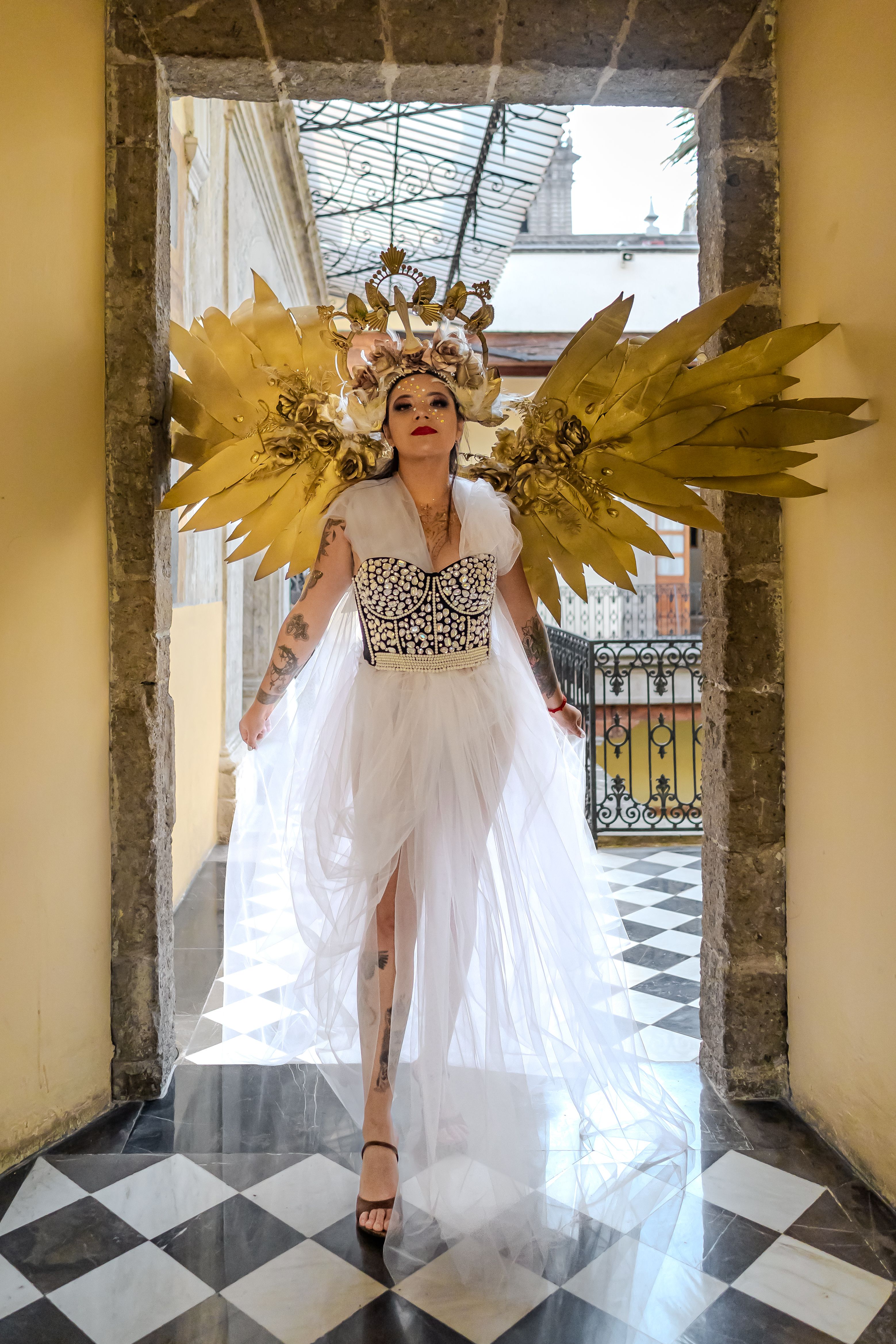 Artistic portrait of a woman in angelic attire with golden wings, indoors in Mexico City.