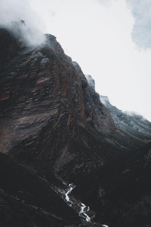 Free Majestic rocky mountain shrouded in clouds and mist under a dramatic sky. Stock Photo