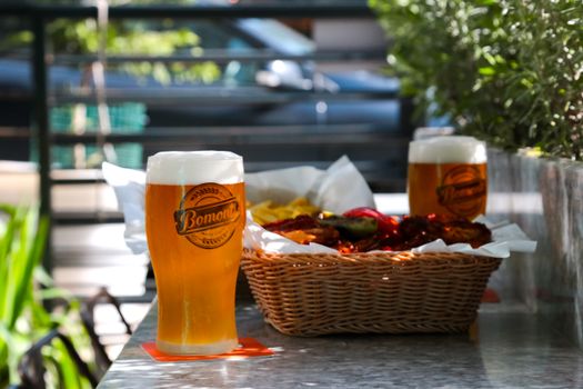 Two glasses of beer and a snack basket on an outdoor table, perfect for a relaxing day.