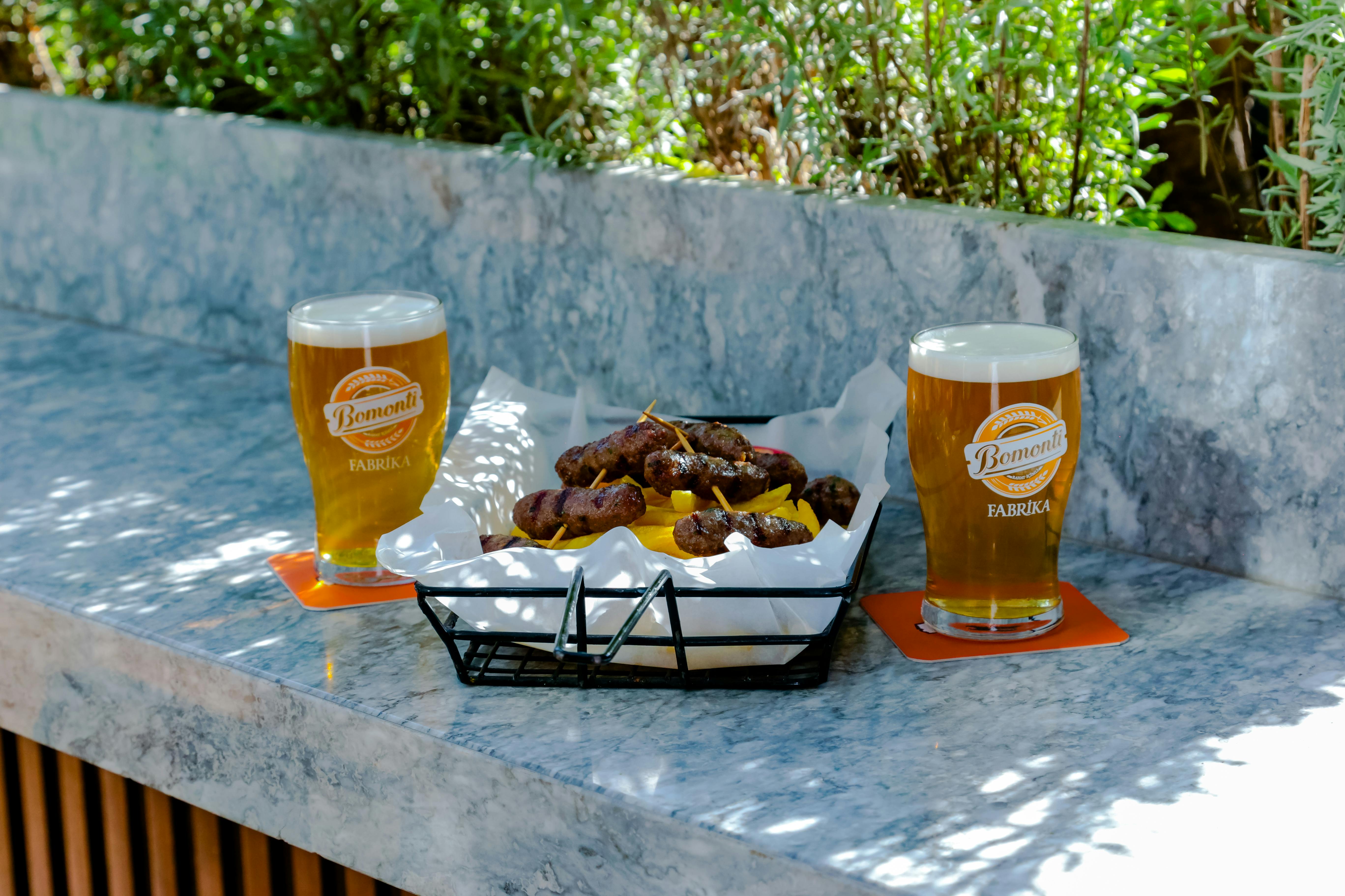 Outdoor setup with two glasses of beer and grilled sausages, perfect for lunch.