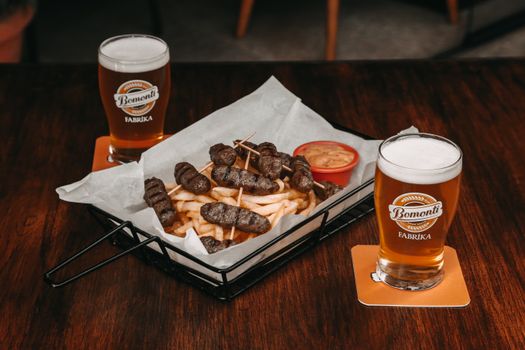 Appetizing platter of meat sausages and fries with refreshing beer glasses on a wooden table.