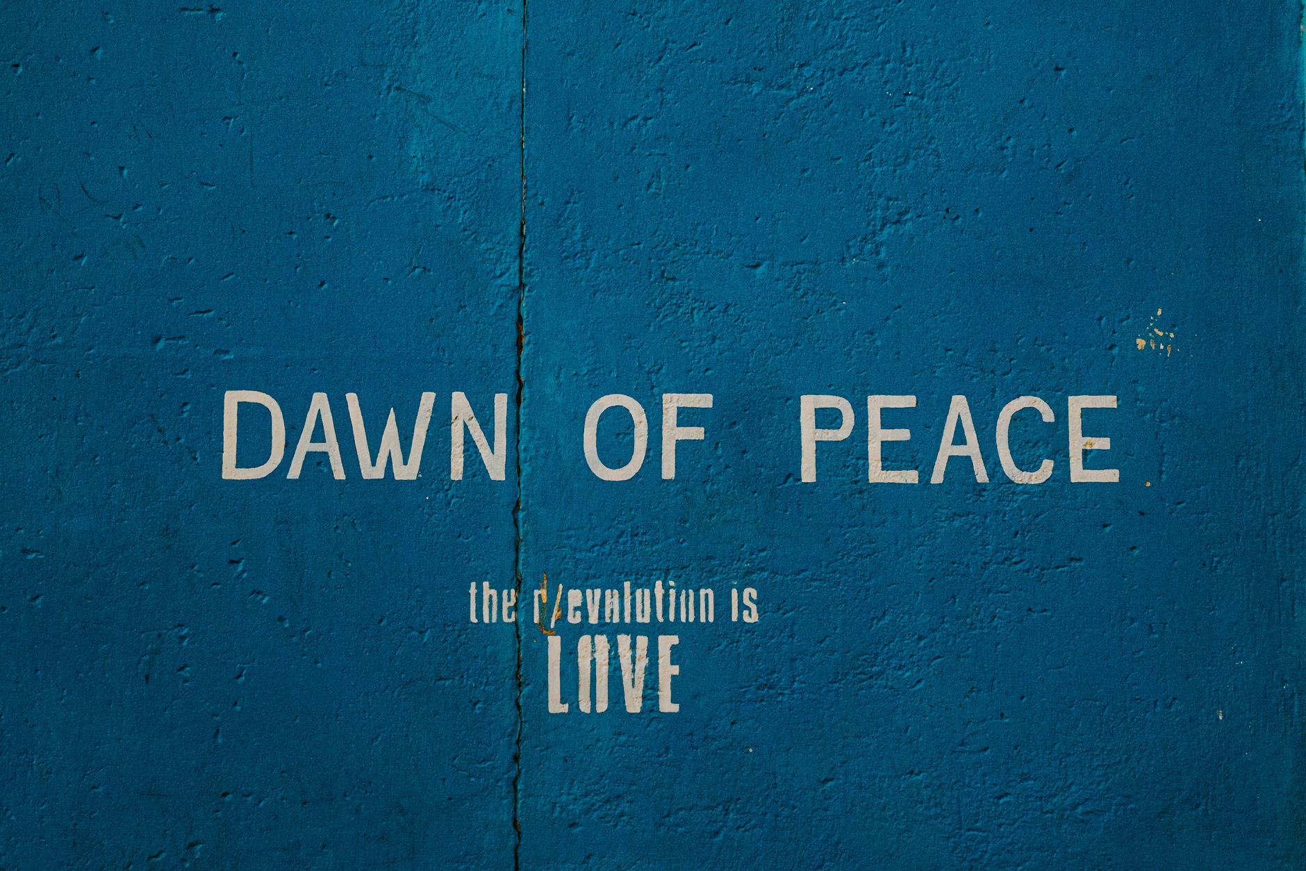 A bold street art mural featuring the message 'Dawn of Peace' on a textured blue wall.