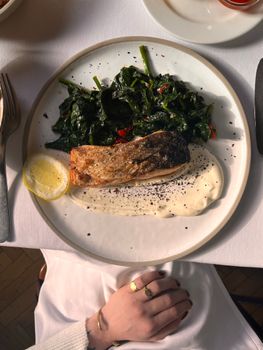 Close-up of cooked salmon with greens and creamy sauce, garnished with a lemon slice on an elegant plate.