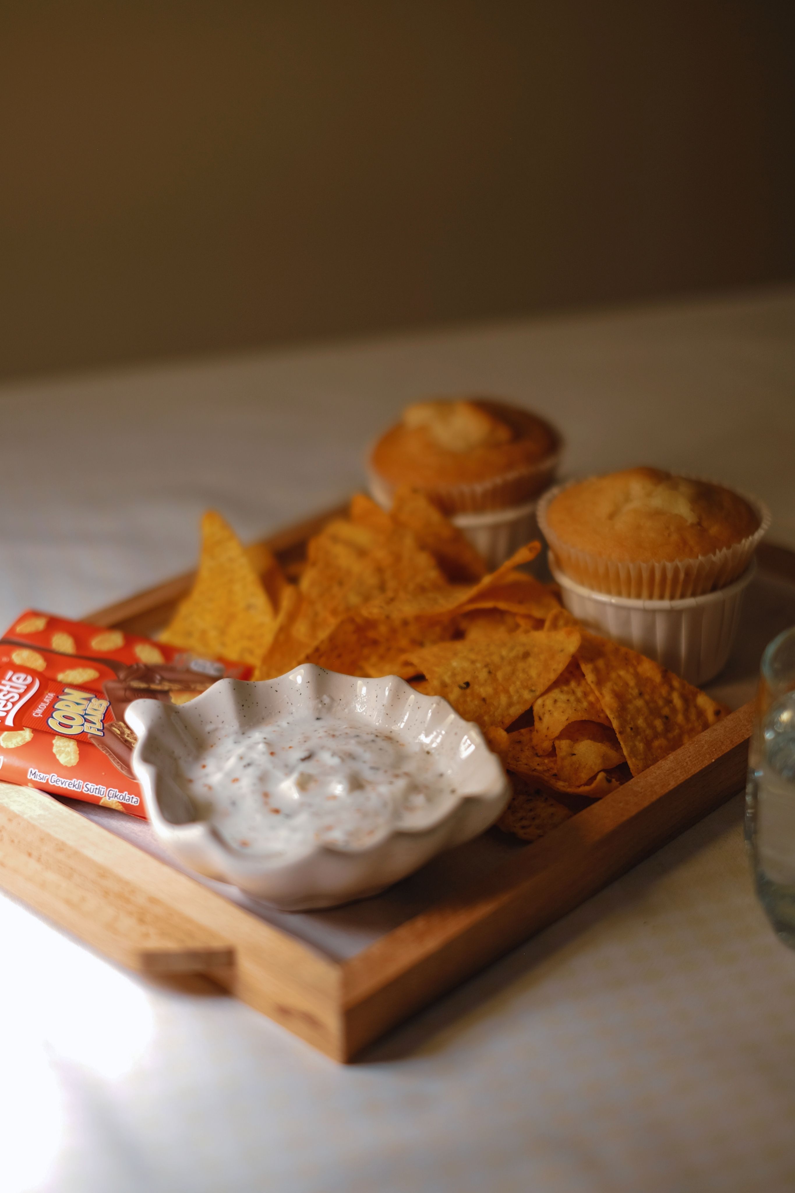Wooden tray with tortilla chips, cupcakes, and dip, perfect for a snack time.