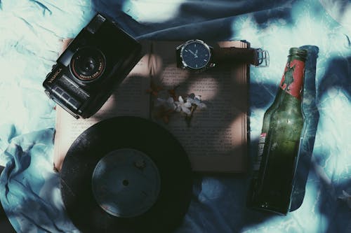 Beer, Vinyl Disk, Flowers, Camera and Wristwatch on Book