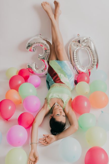 morning routine proven - Woman celebrating 30th birthday with colorful balloons in a studio setting.