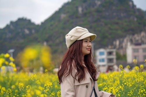 Model in a Beige Newsboy Cap and Coat Among Yellow Flowers