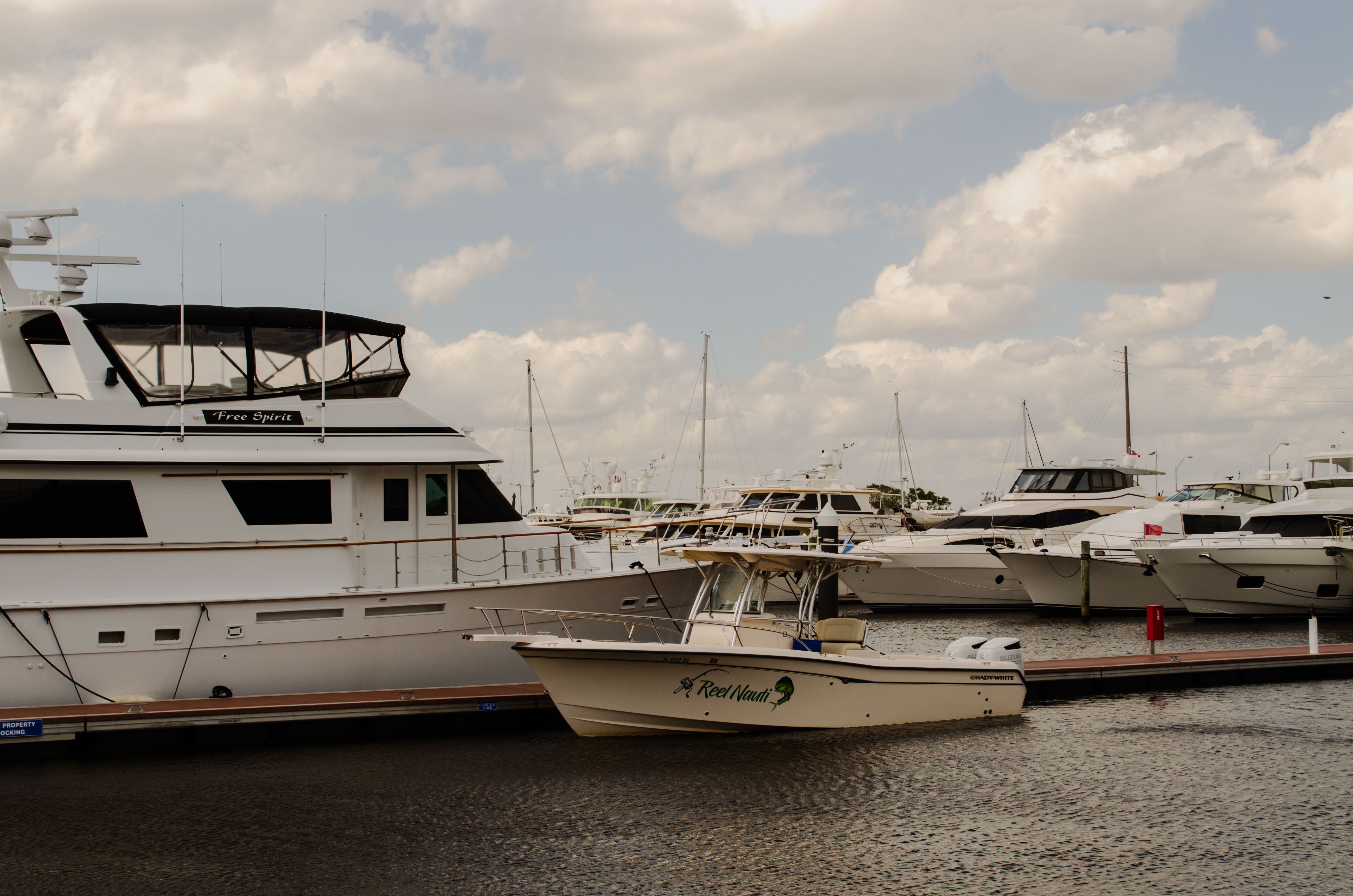 A tranquil marina with yachts docked under a picturesque cloudy sky.