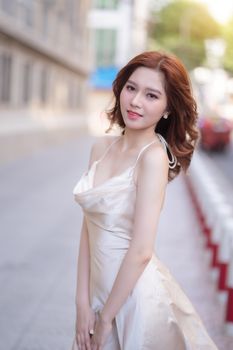 An elegant woman in a silk dress poses on a sunny city street, exuding glamour and style.