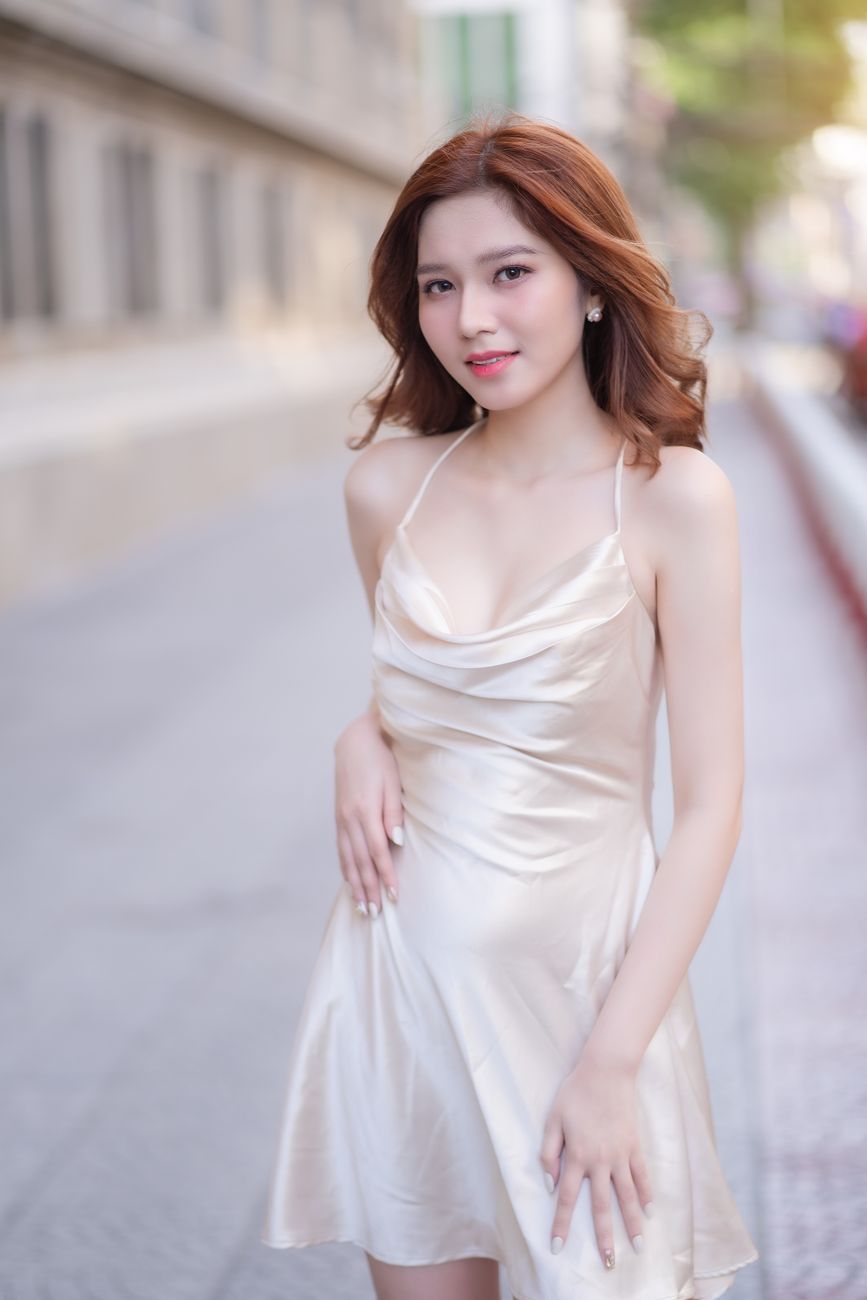 Elegant woman in a satin dress posing outdoors with a confident smile, showcasing fashion and style.