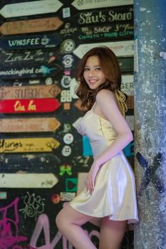 Elegant woman in silk dress posing by colorful urban signs wall.