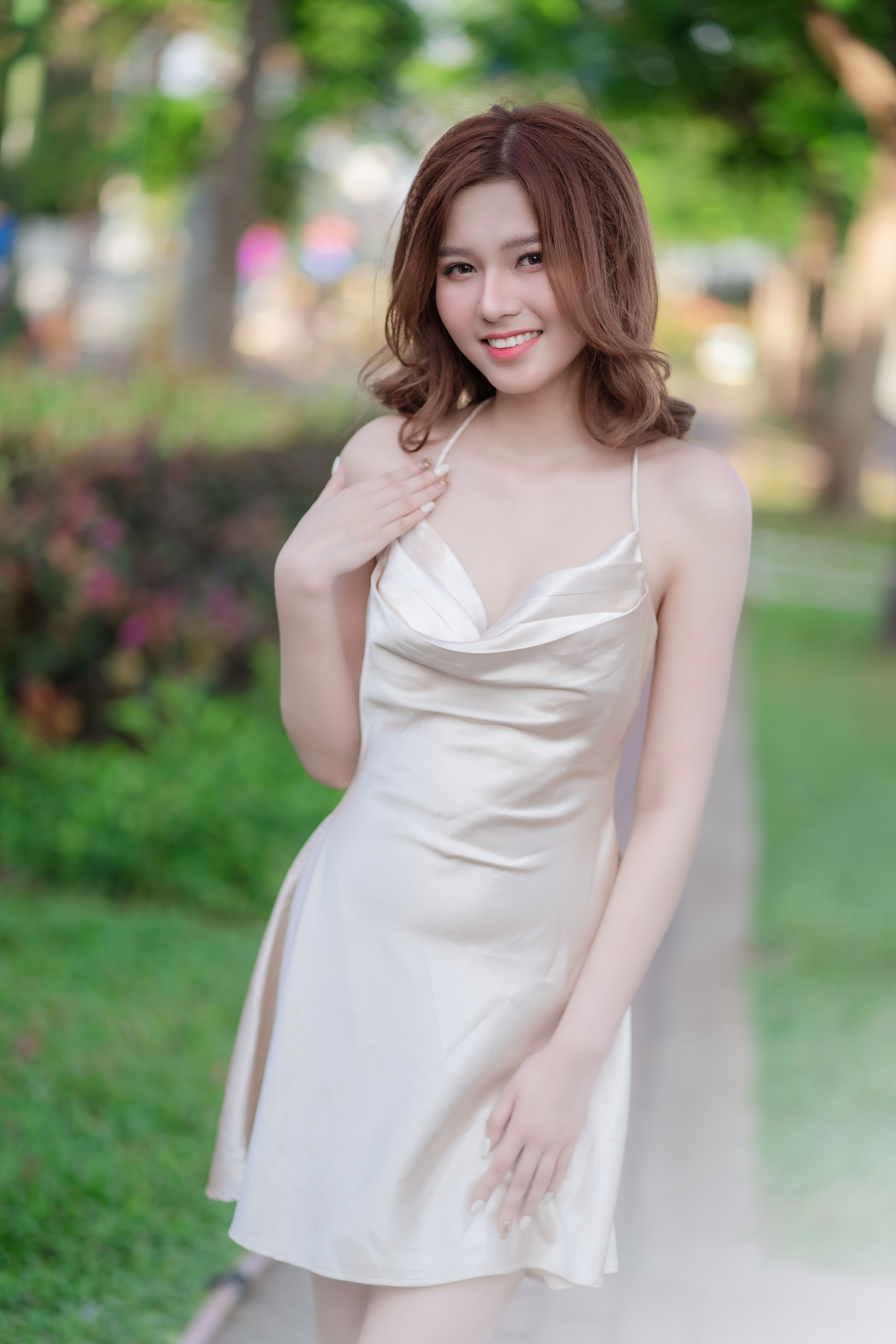 Smiling woman in a satin white dress posing gracefully outdoors.