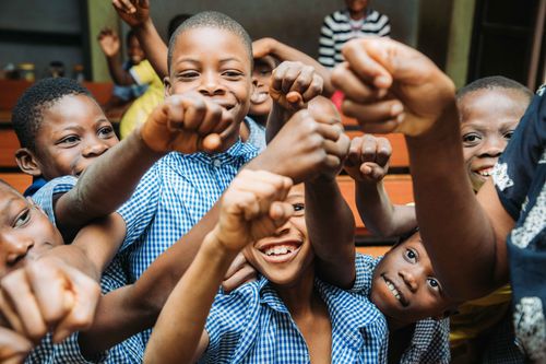 Free Group of smiling African children showing unity with raised fists in a classroom setting. Stock Photo