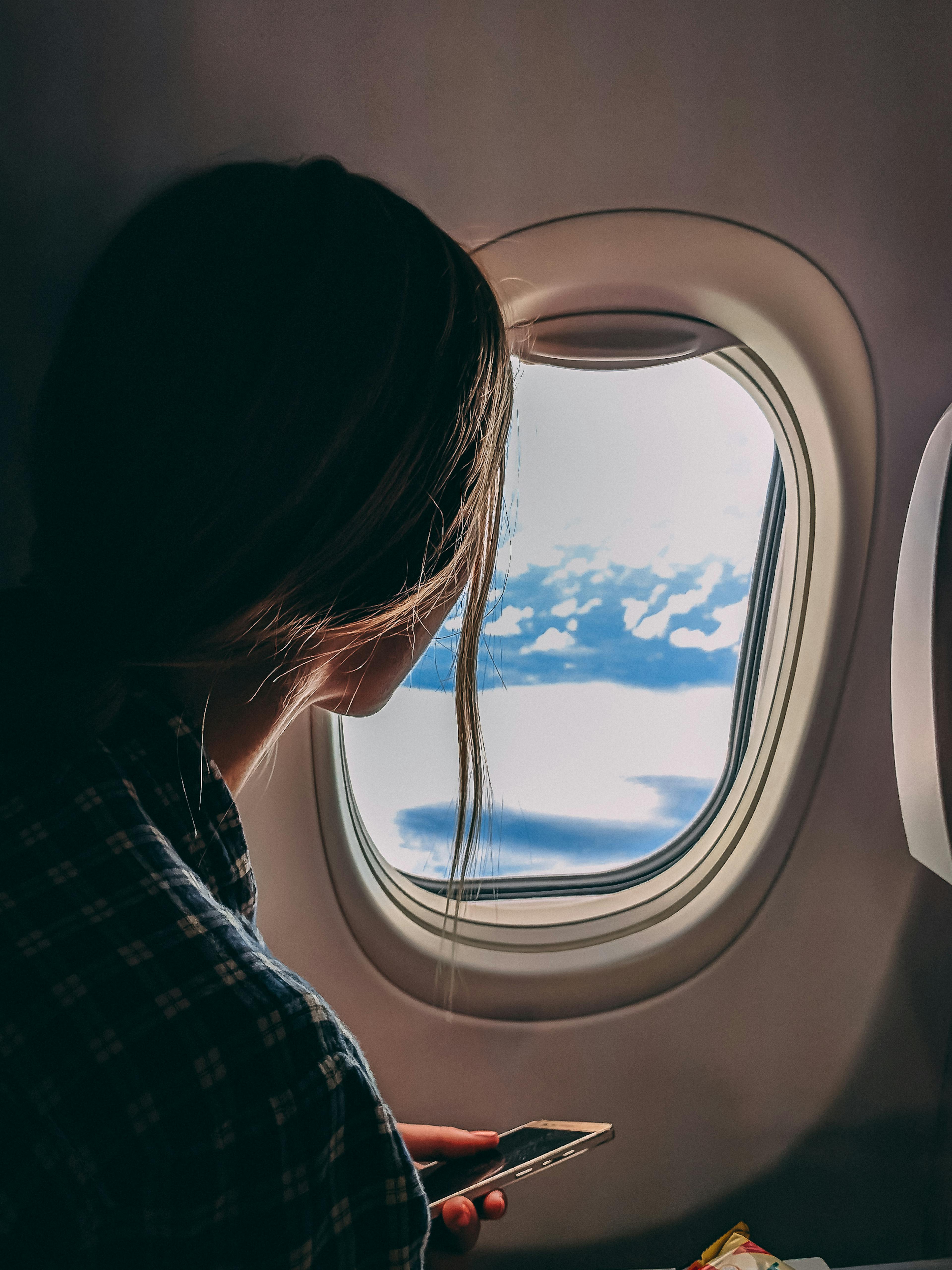 A woman looks out an airplane window, capturing a serene view of clouds and sky during a flight.