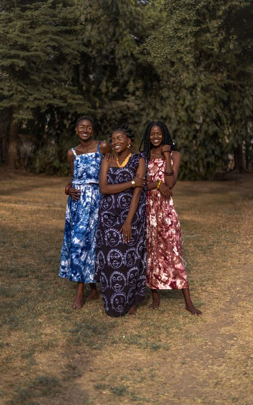 Free Three smiling women in colorful traditional dresses standing outdoors in a grassy area with trees. Stock Photo