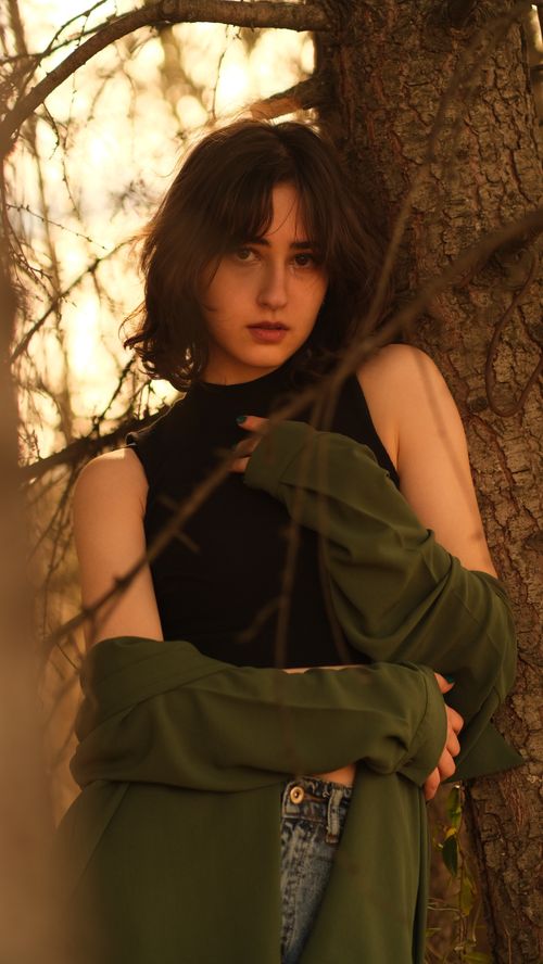 Free A young woman with bangs poses outdoors against a tree wearing casual clothing. Stock Photo