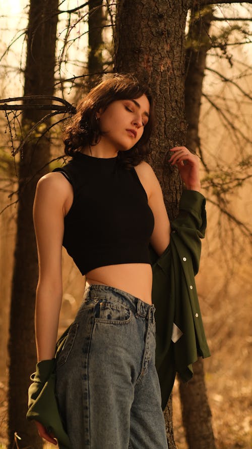 A woman in jeans and a crop top posing in the woods