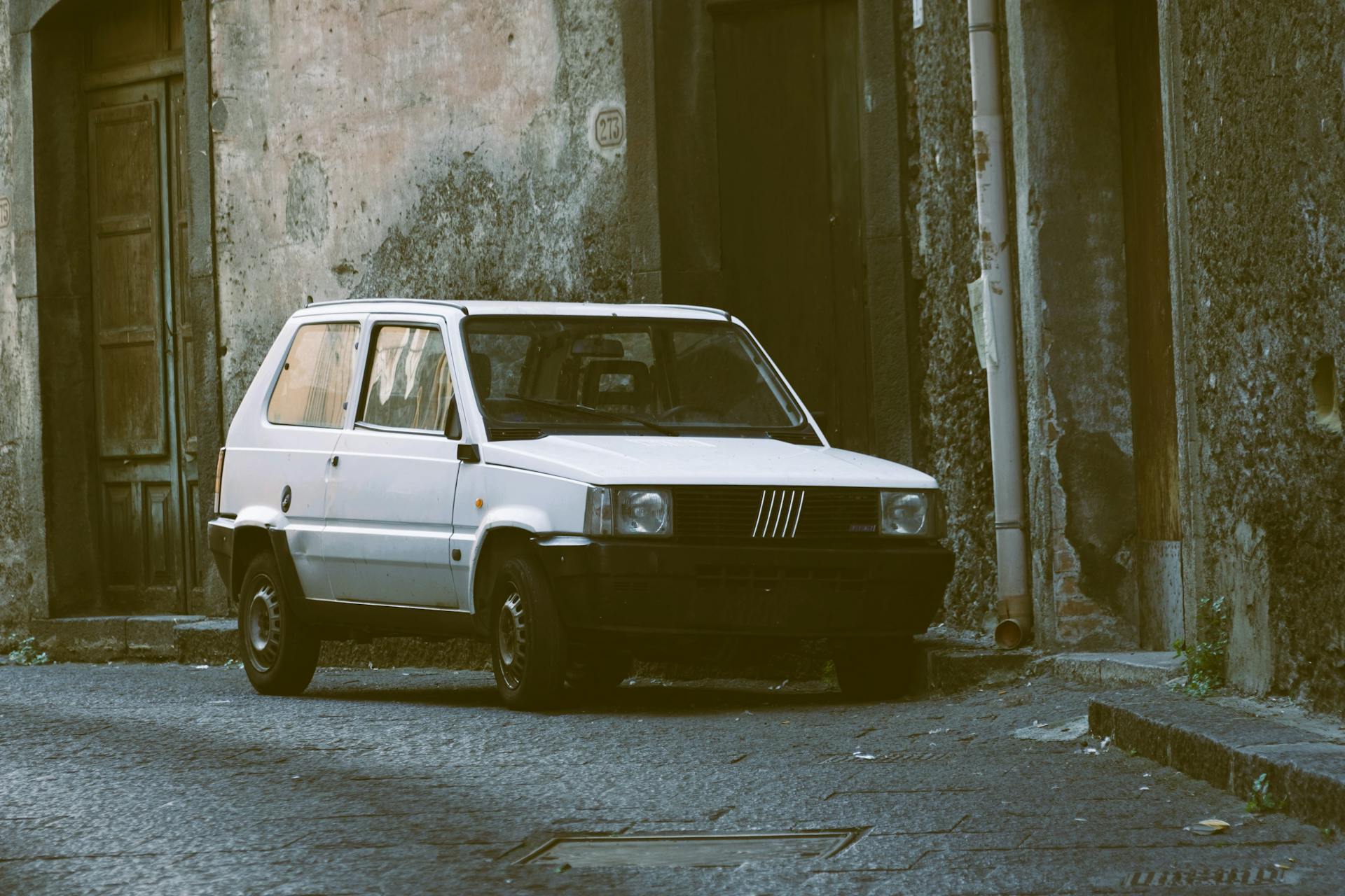 A classic white Fiat Panda parked in a narrow urban alley with vintage charm.