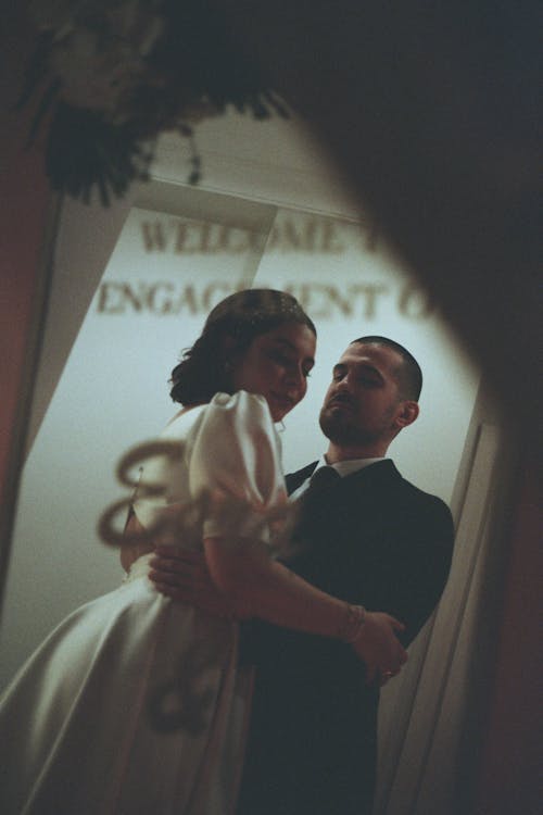 A bride and groom embrace in front of a sign