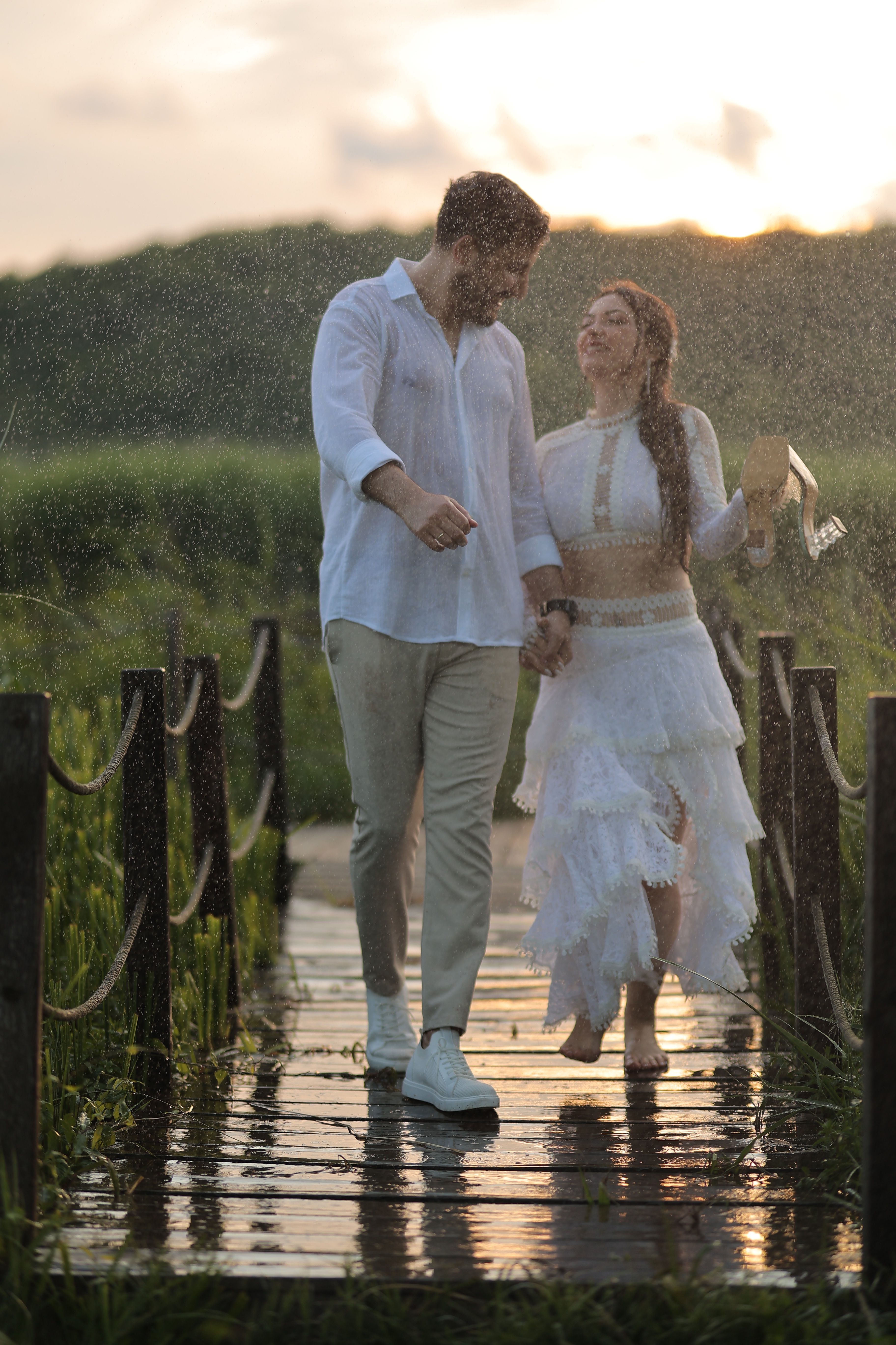 Couple holding hands on a rainy footbridge, exuding romantic vibes in a rural setting.
