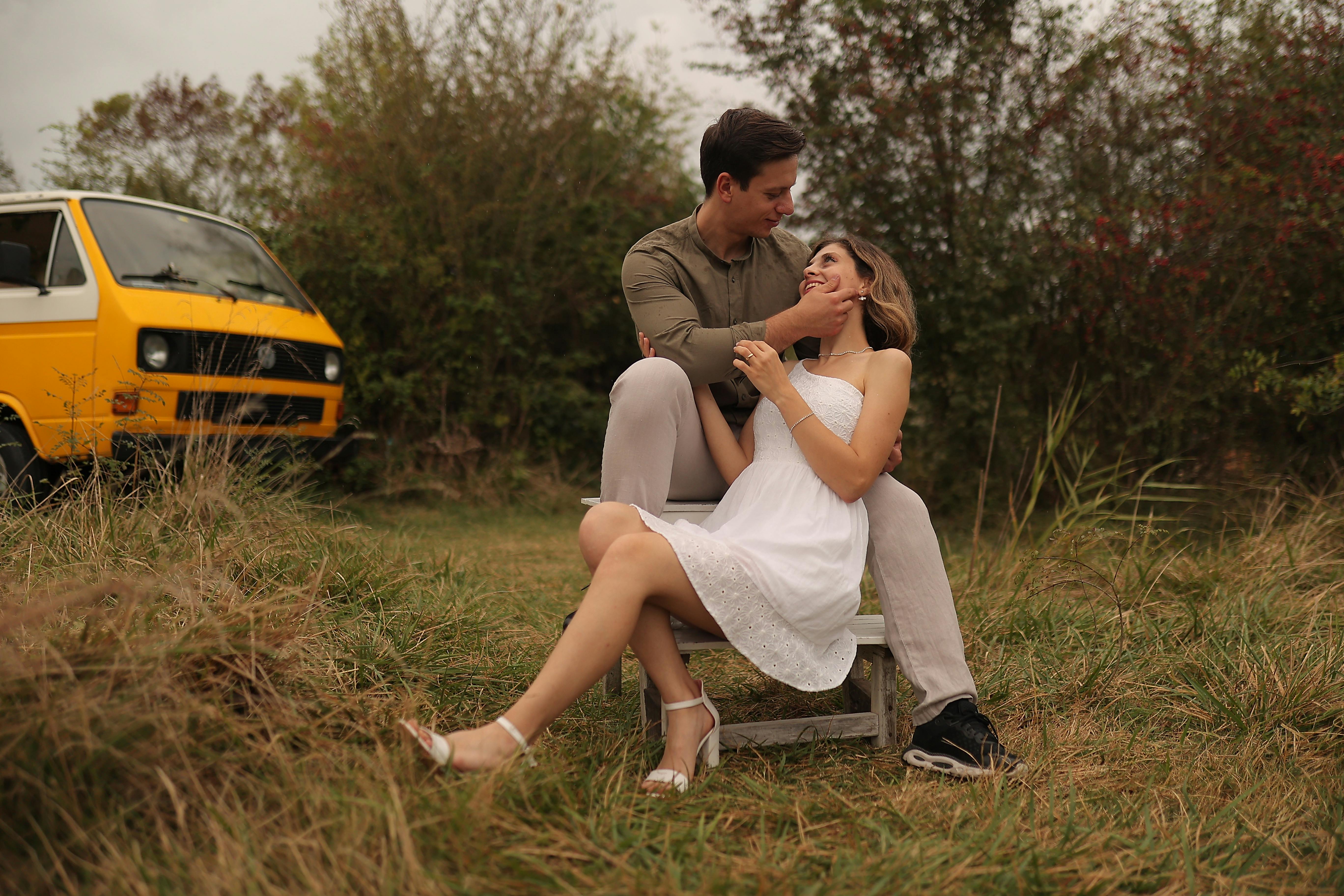 A loving couple embracing in nature next to a yellow van, evoking romance and adventure.