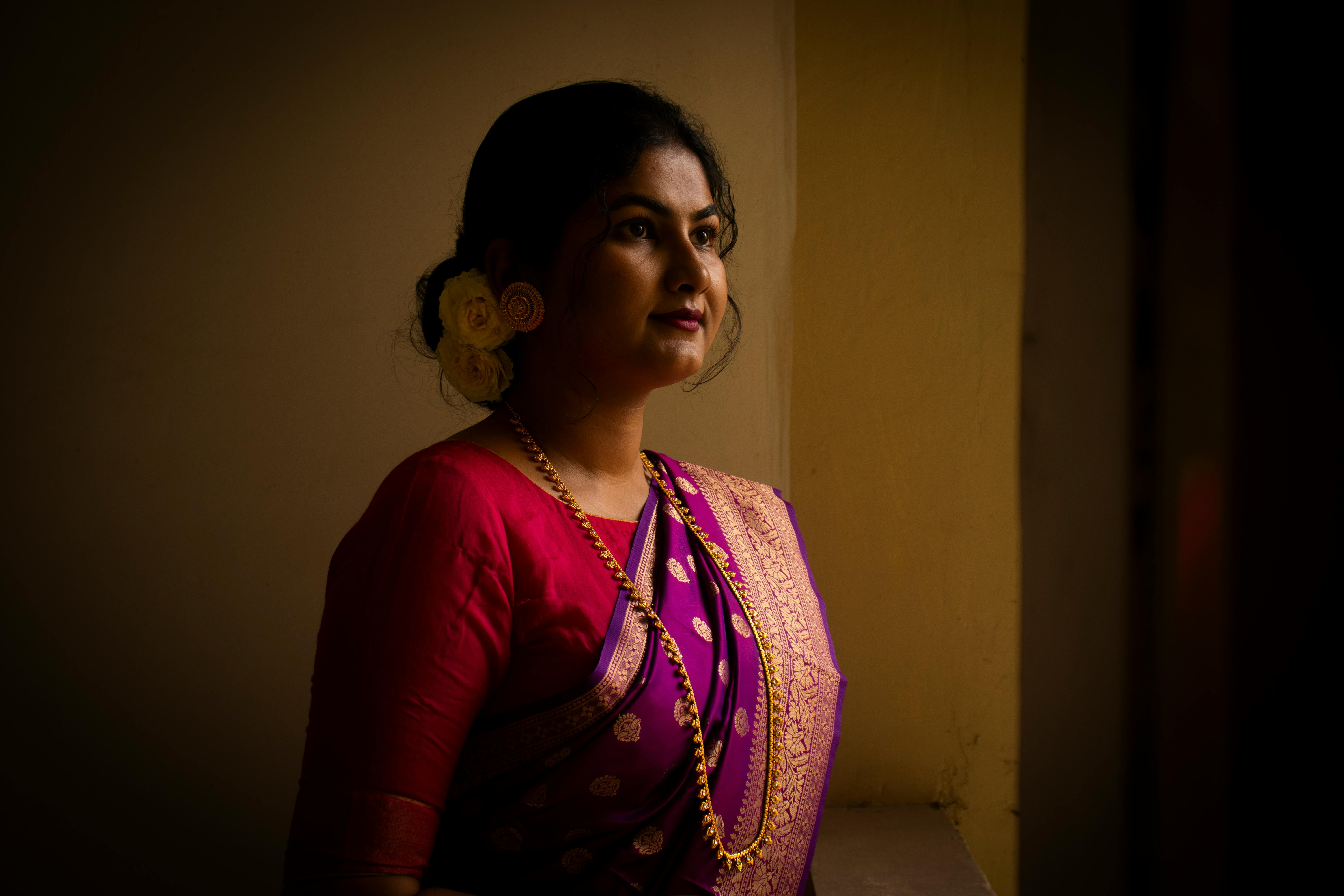 Elegant Indian woman in a purple saree with gold embroidery, gazing thoughtfully indoors.