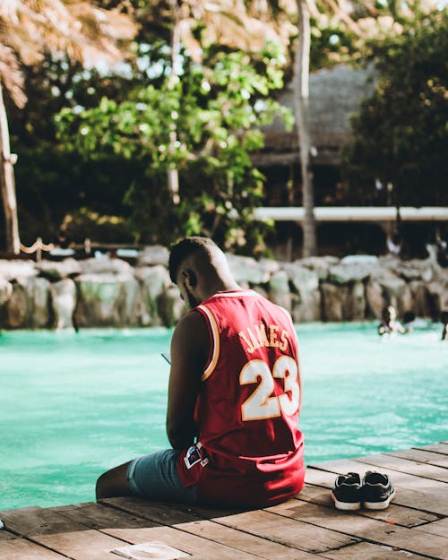男子身穿紅色勒布朗·詹姆斯23球衣坐在水體附近的碼頭上