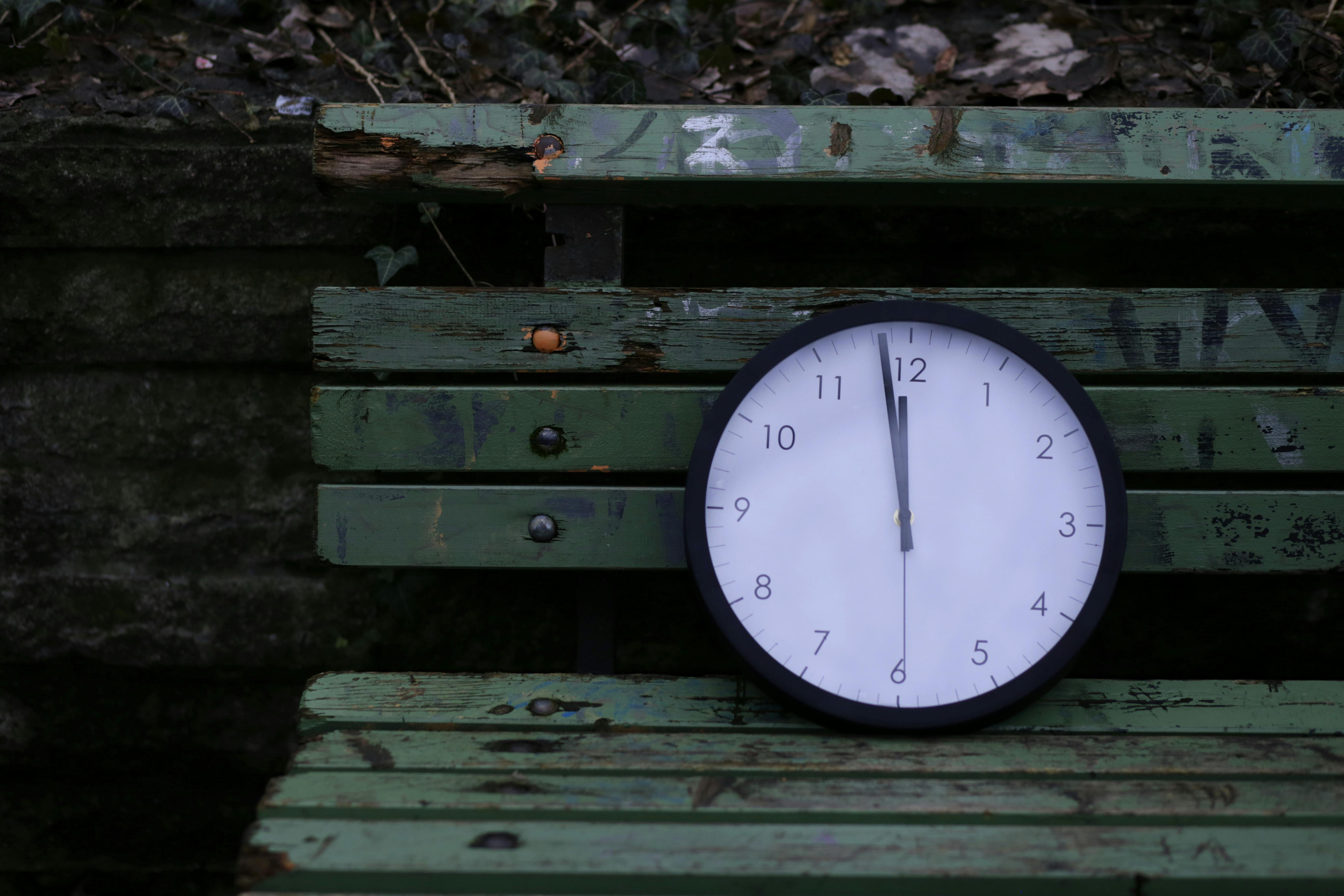 Close-up of an analog clock on a rustic green wooden bench outdoors.