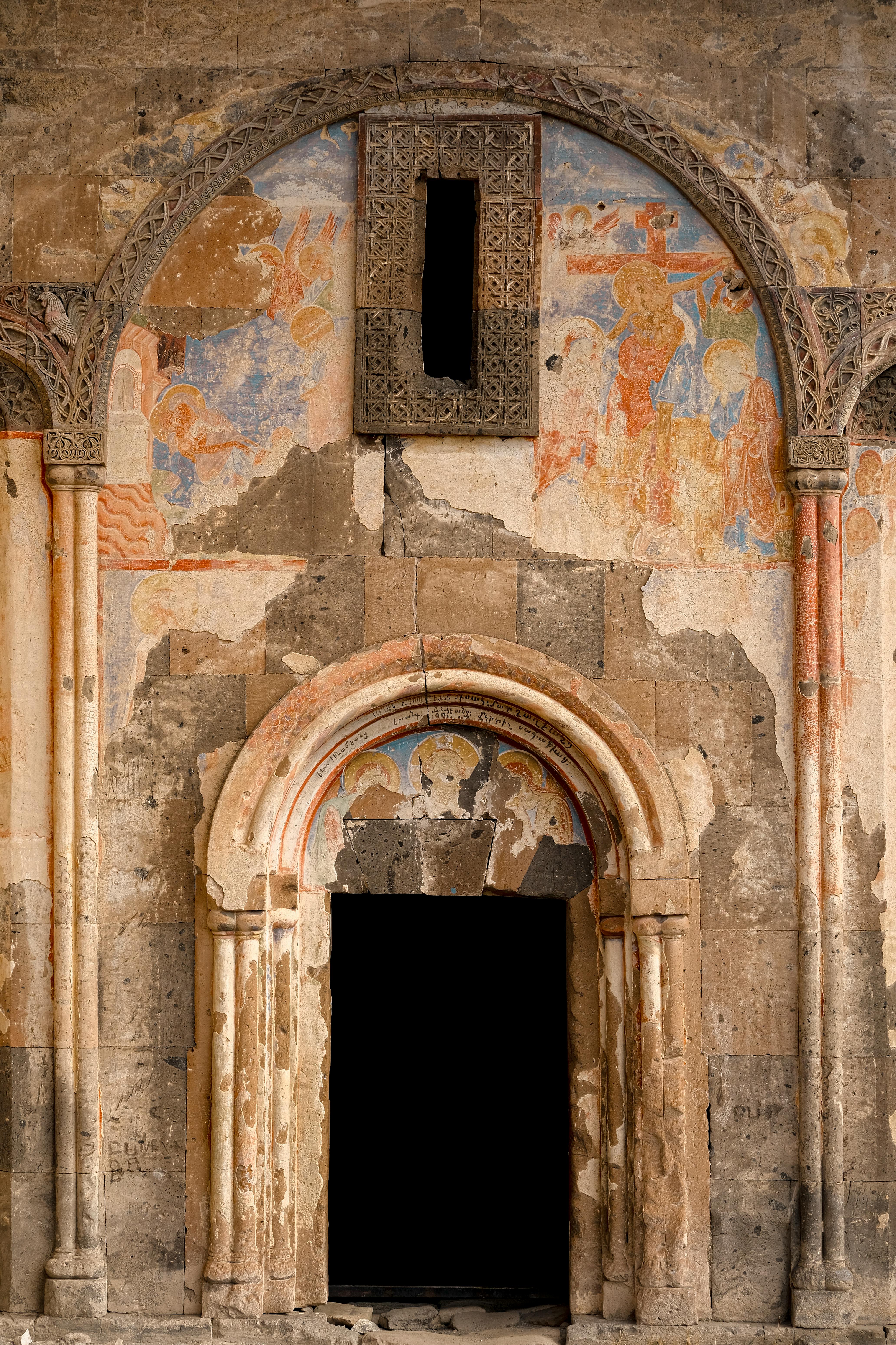 Historic Armenian church entrance featuring faded frescoes and intricate arches in Turkey.