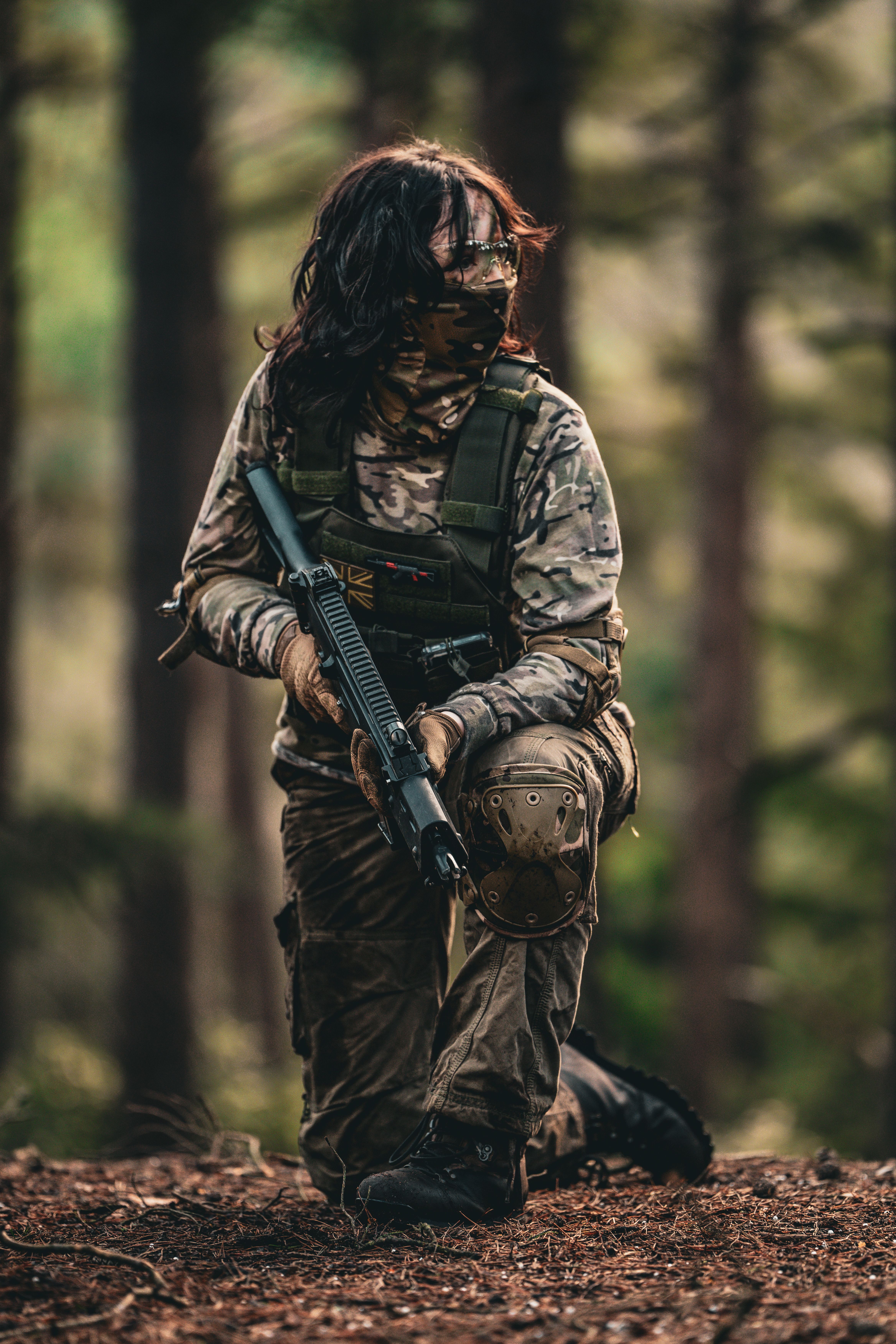 Person in tactical gear and camouflage engaged in airsoft skirmish outdoors.