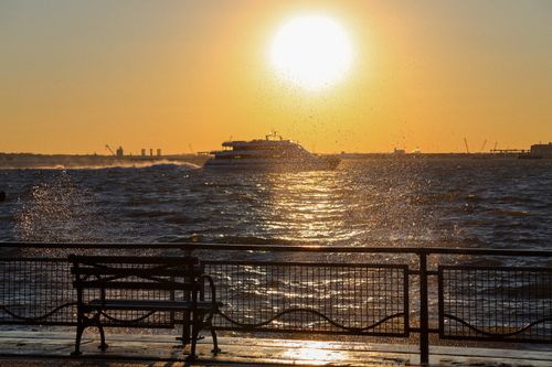 Free A serene scene capturing a bench silhouetted against the golden sun setting over the ocean. Stock Photo