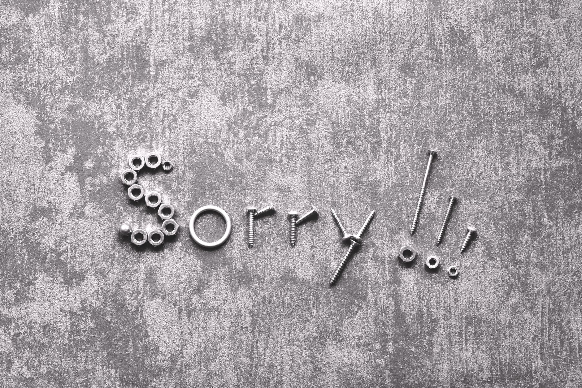 Ingenious display of apology with the word 'Sorry' crafted out of nuts and bolts on a textured surface.