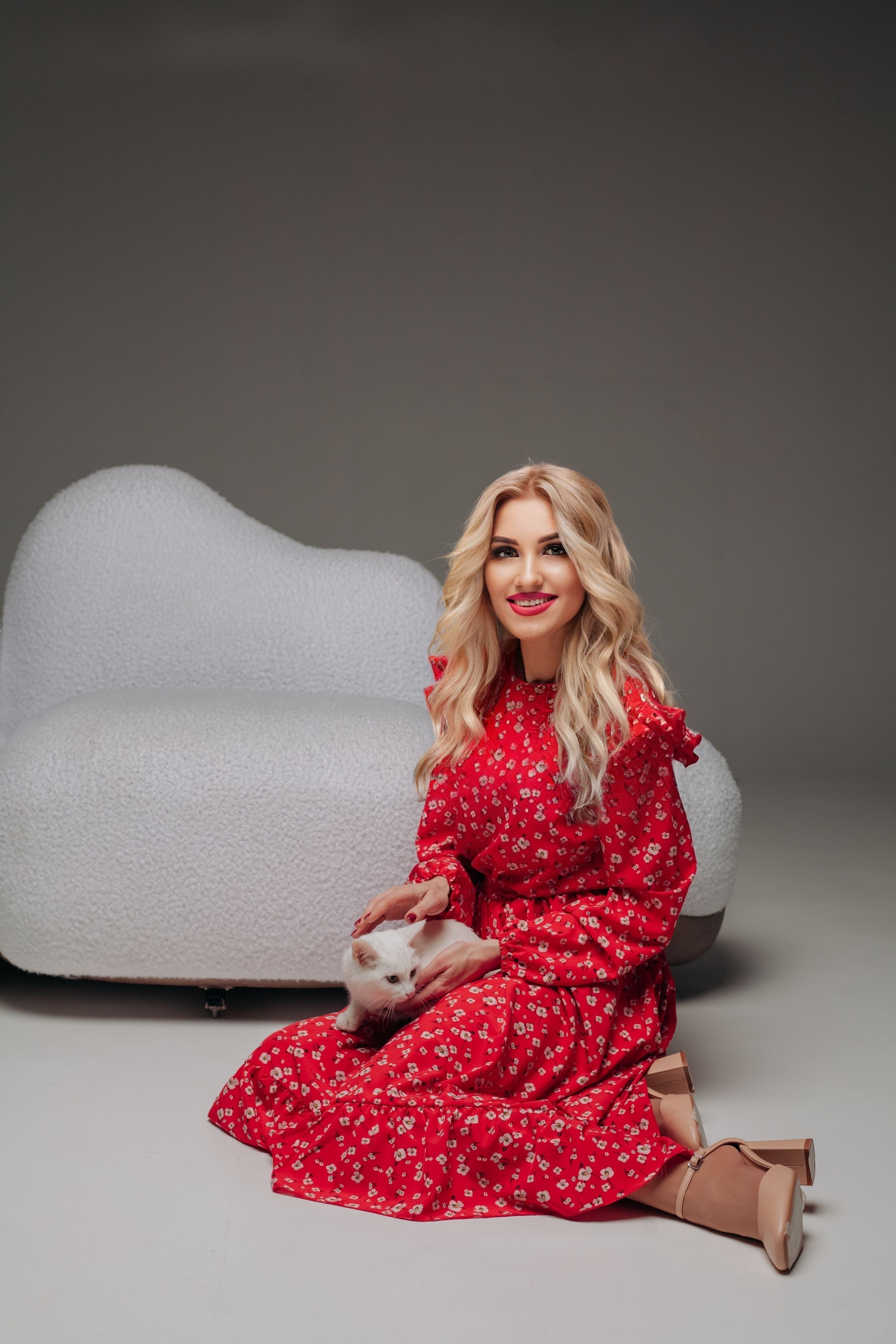 Blonde woman in a red dress posing elegantly with a cat in a studio setting.