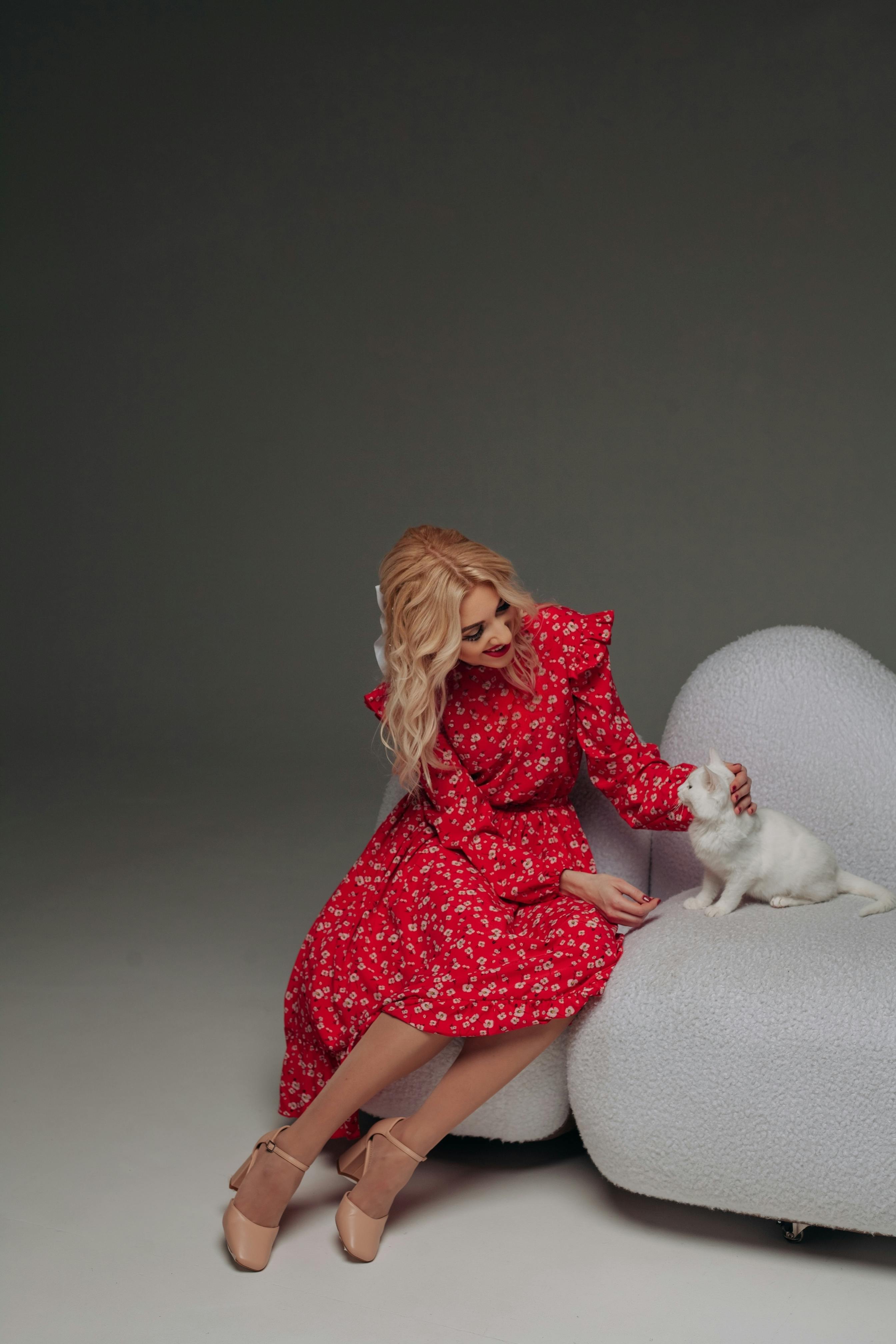 A stylish woman in a red dress poses with a white cat in a studio setting.
