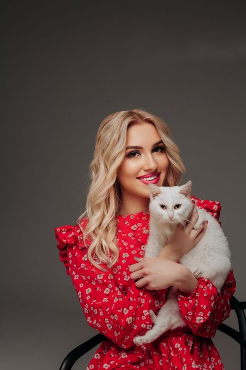 Free Charming woman smiles while holding a white cat during a studio shoot. Stock Photo