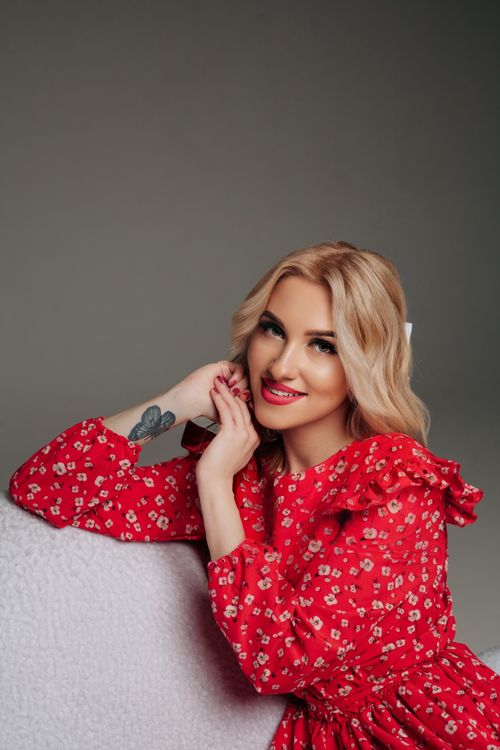 Free Young woman with blonde hair elegantly posing indoors in a red dress. Stock Photo
