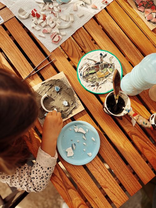 Free Top view of a child creating a mosaic art piece with colorful tiles on a wooden table. Stock Photo