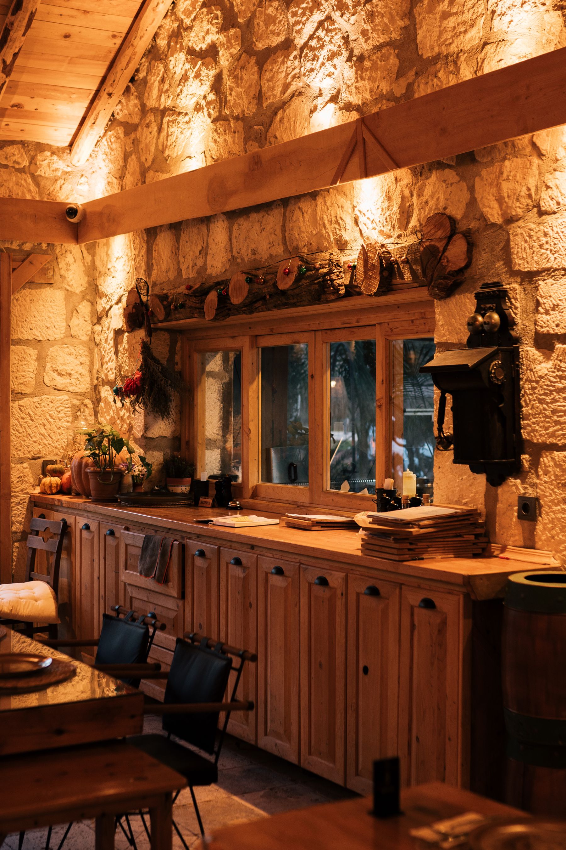 Rough stone walls, exposed timber beams and paneled wood cabinetry beneath a wooden window