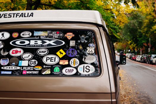 A vintage van adorned with various travel stickers parked on an autumn street with colorful foliage.