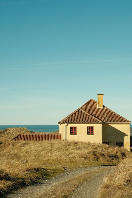 A quaint rural house with a red tiled roof against a clear blue sky, surrounded by grass.