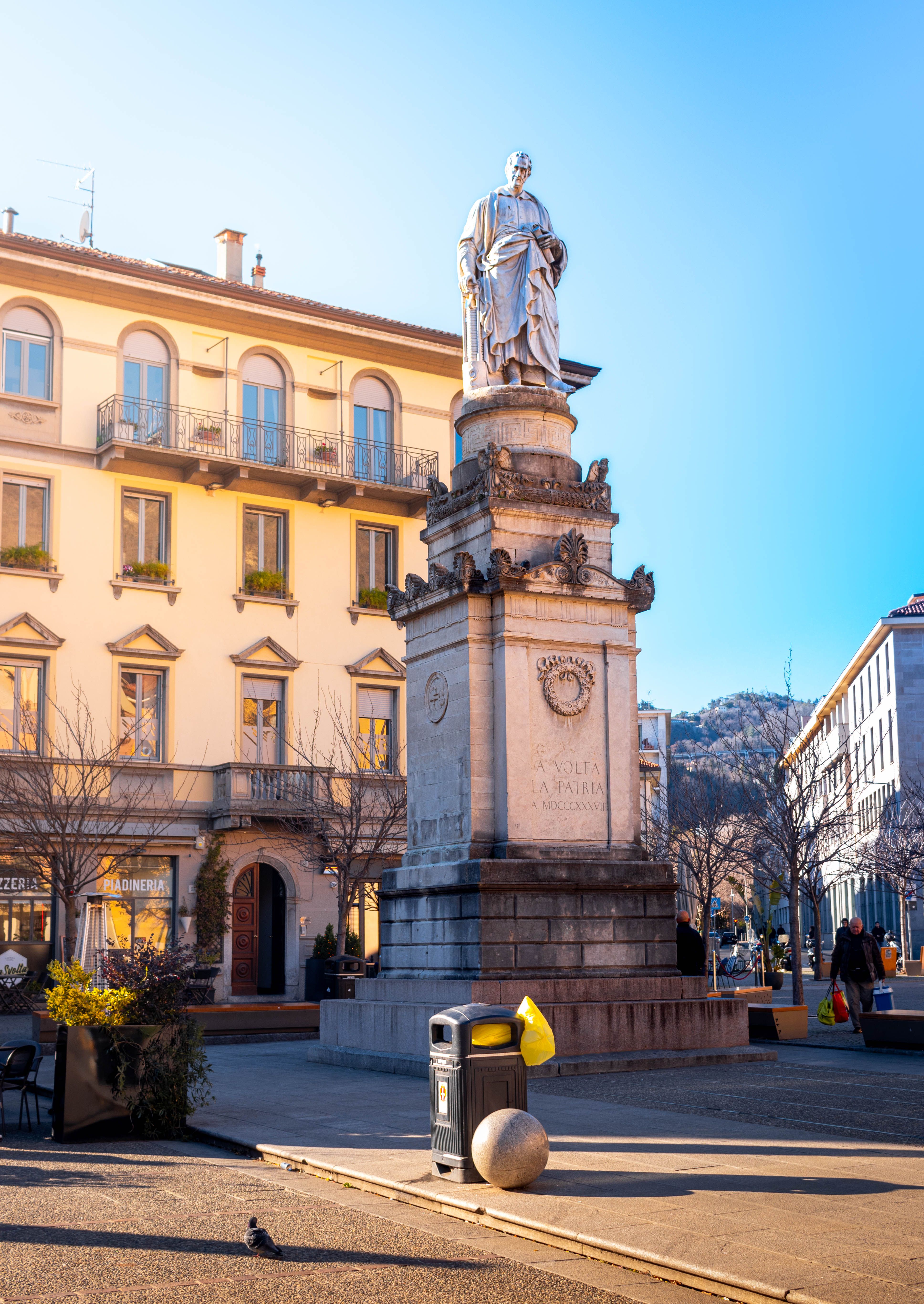Statue of Alessandro Volta in a vibrant city square in Como, Italy during a clear day.