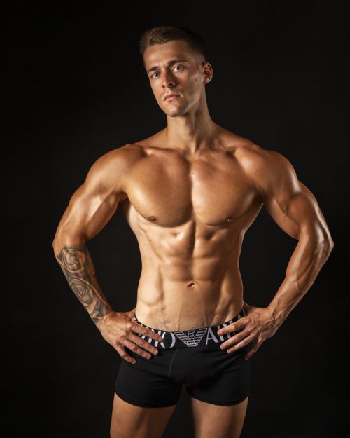 Free Portrait of a muscular male model with tattoos standing in a studio against a black background. Stock Photo