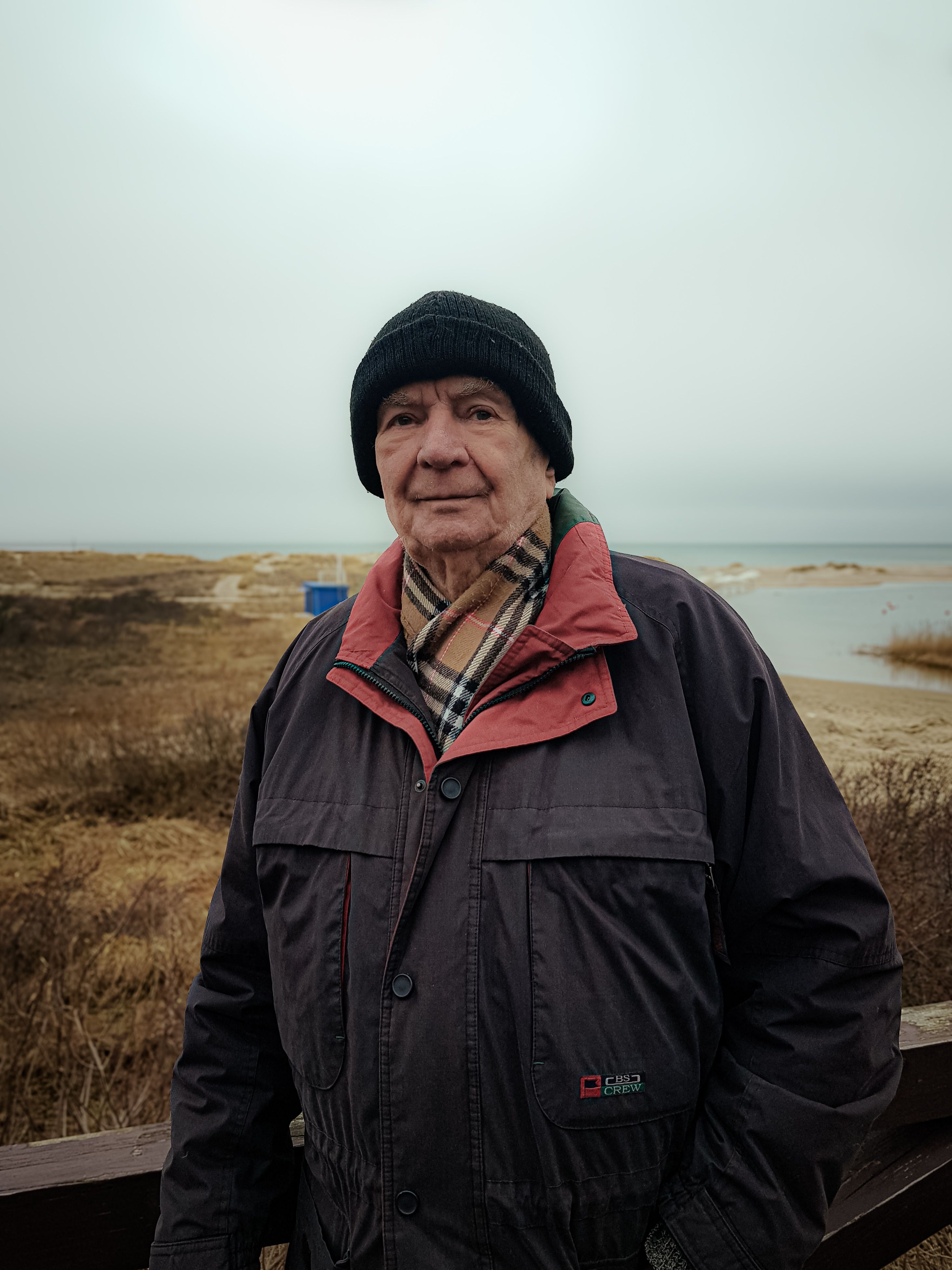 Senior adult in a coat and hat by a lake on a peaceful fall day.
