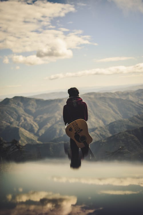 Mężczyzna Niosący Gitarę, Stojąc, Patrząc Na Wzgórza