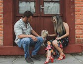 一对夫妇坐在砖街上，对着他们的狮子狗微笑